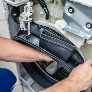 Technician installing a black appliance belt inside a washing machine.