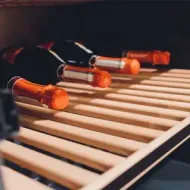 Several wine bottles resting on wooden shelves inside a wine cooler
