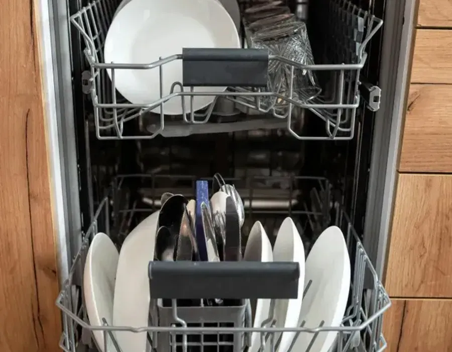 Open dishwasher with clean white dishes and plates loaded in the racks