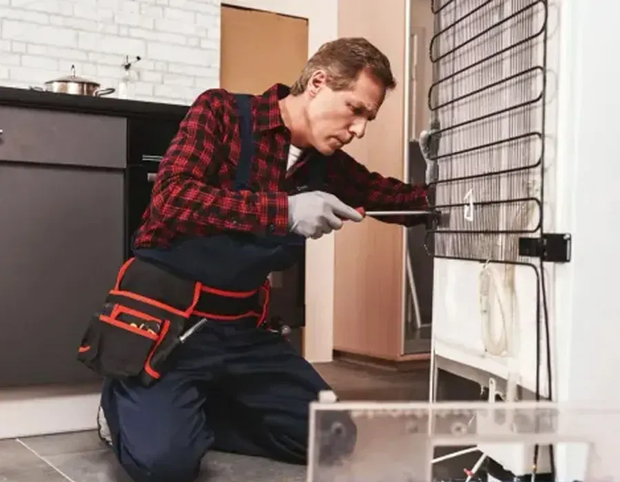 Person kneels beside a wire cage, working with tools in a room with a white brick wall and cabinets.