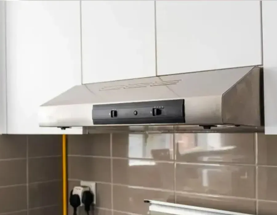 Stainless steel kitchen range hood above a tiled backsplash and white cabinets