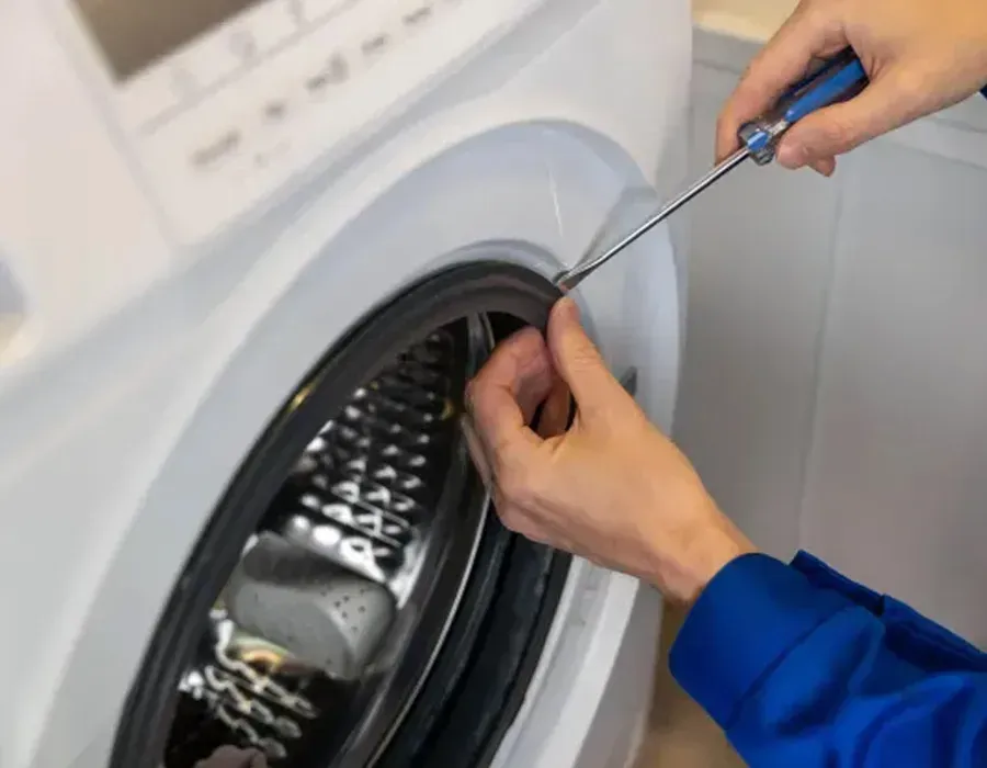 Hands using a screwdriver to repair a washing machine drum