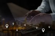 Hands typing on a laptop with glowing location pins over a dark digital map interface