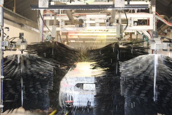 Car wash tunnel with hanging black brushes spraying water around a white vehicle