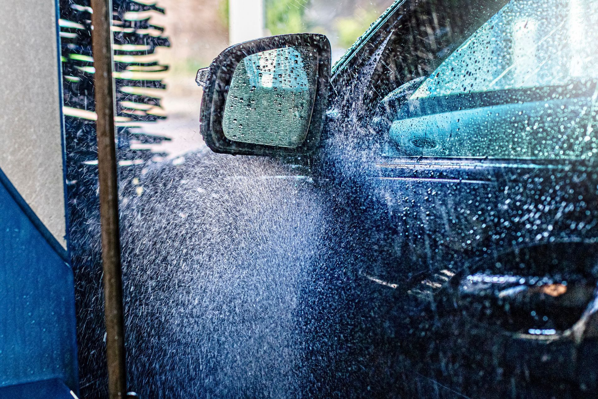 Car being sprayed with water at a car wash, side mirror visible through splashes