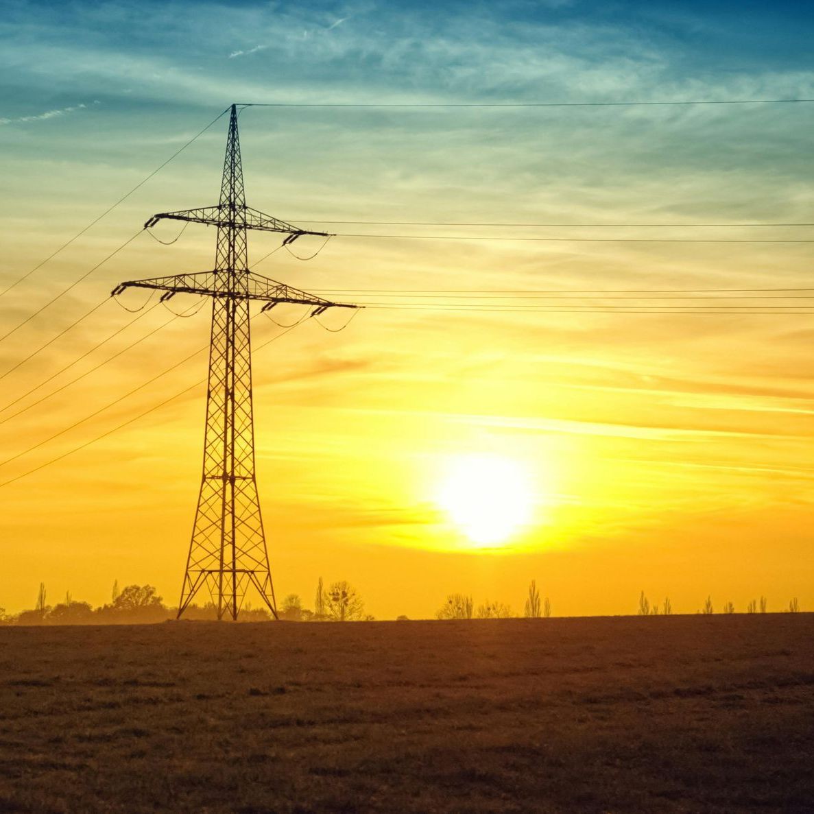 Tramonto su un campo, con un'alta torre dell'alta tensione che si staglia contro il sole splendente.