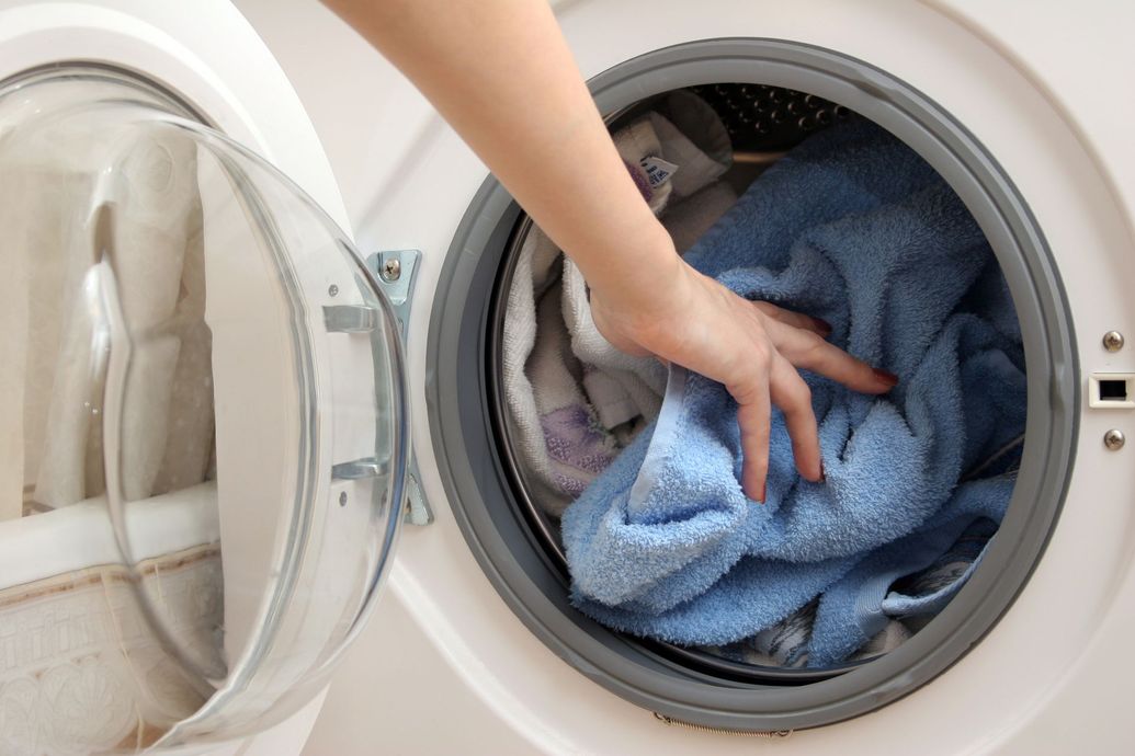 Hand reaching into a front-loading washing machine with blue laundry inside