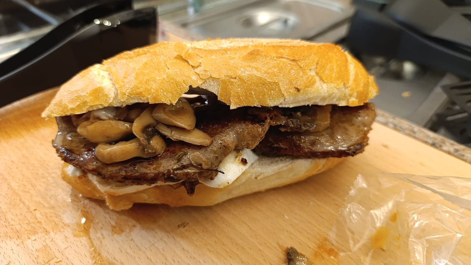 Panino con carne e funghi su un tagliere di legno.
