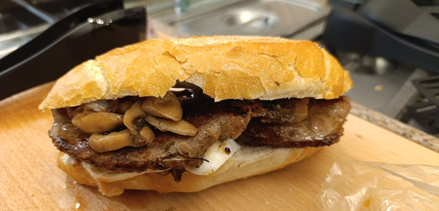 Panino nero con polpo, lattuga e salsa su un piatto nero.