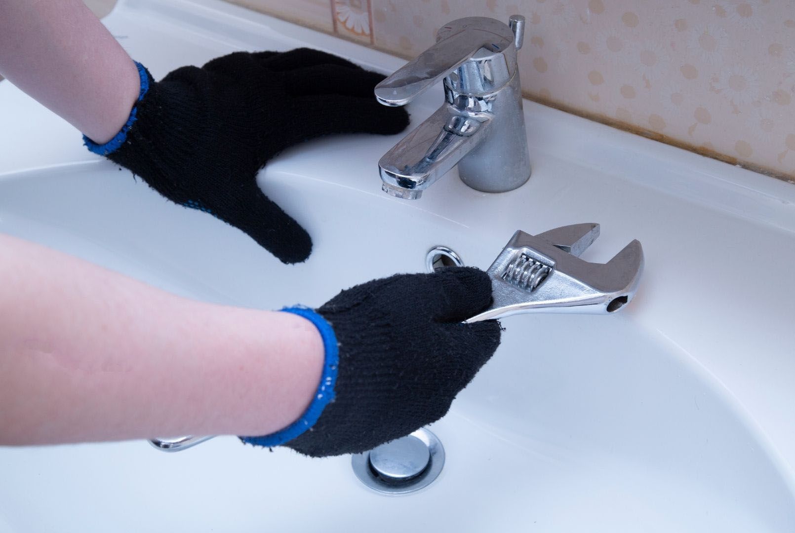 A man is fixing a sink faucet with a wrench.