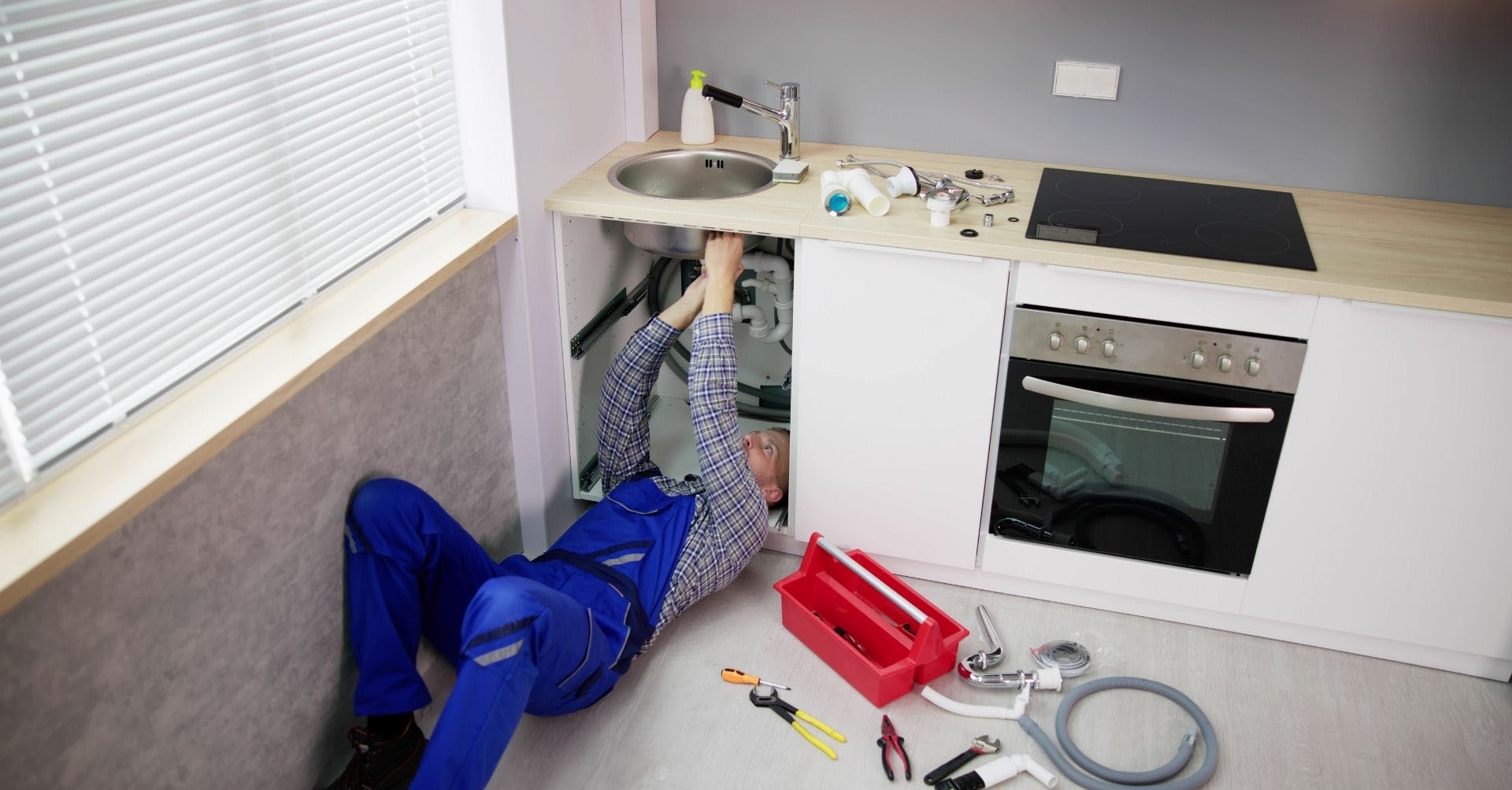 A plumber is laying on the floor fixing a sink in a kitchen.