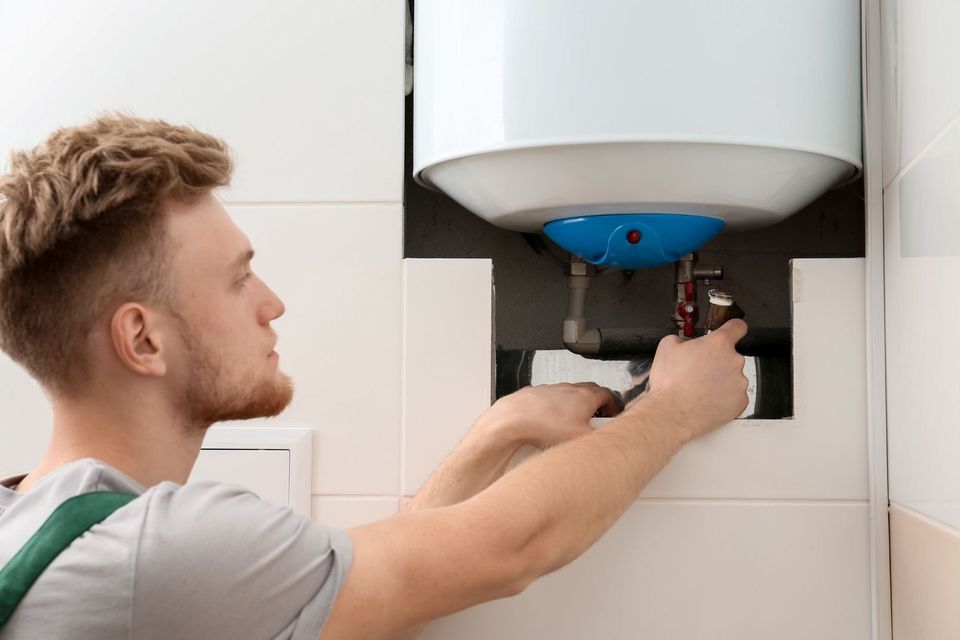 A man is fixing a water heater in a bathroom.
