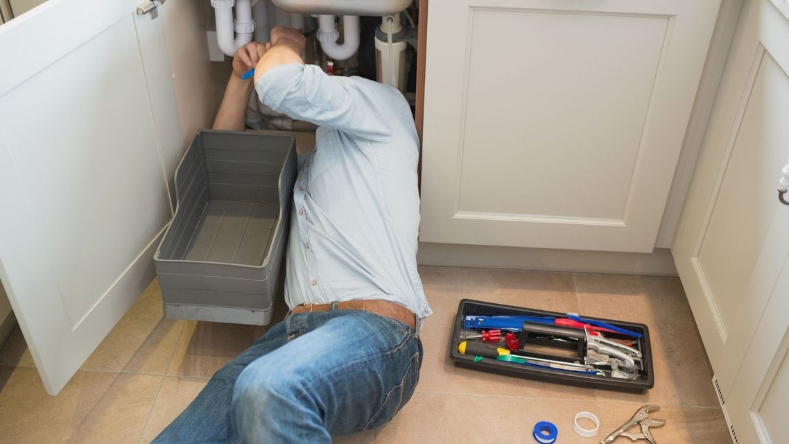 A man is kneeling on the floor fixing a sink.