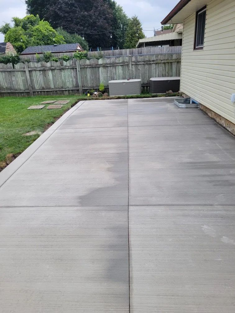 Smooth concrete patio recently installed in a backyard beside a yellow home