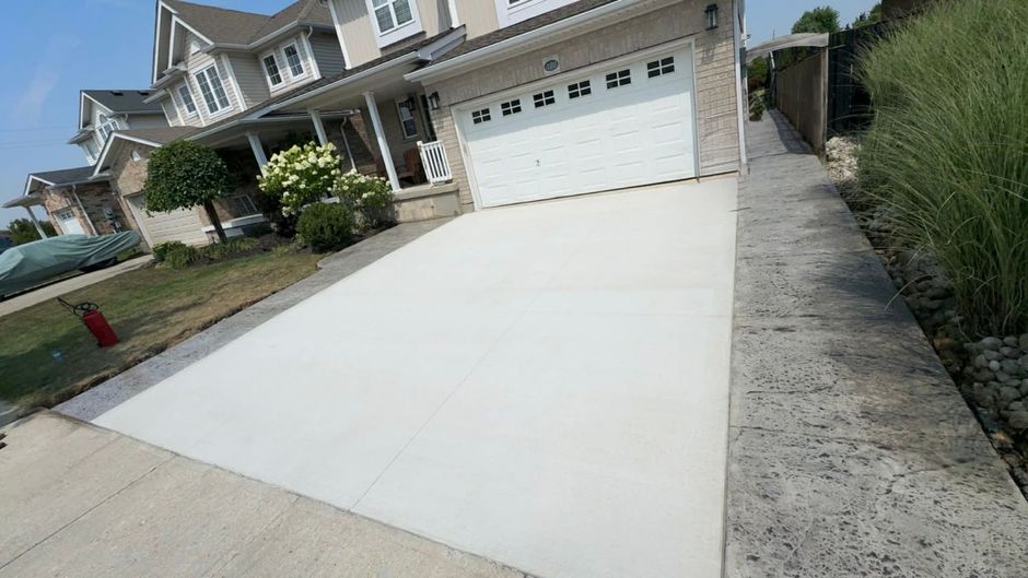 Wide driveway leading to a two-car garage in a suburban house with hedges and a concrete walkway