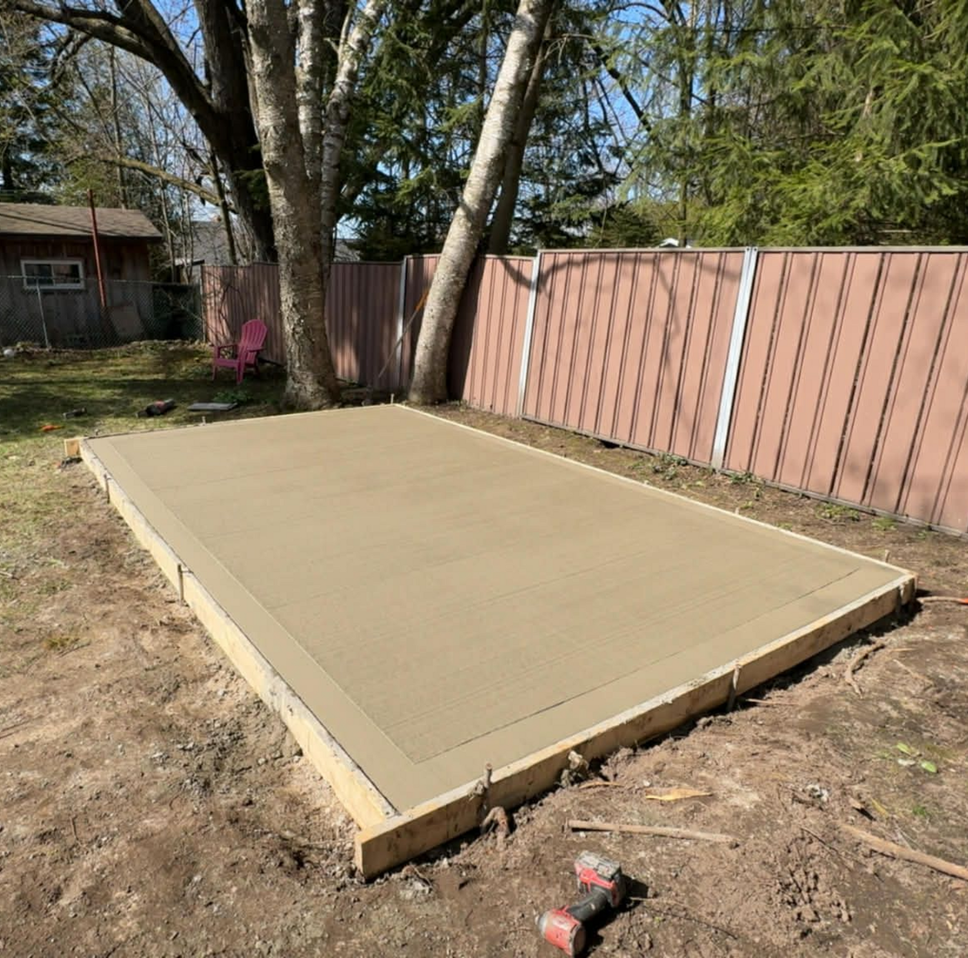 Concrete slab foundation in a backyard beside a fence and trees.
