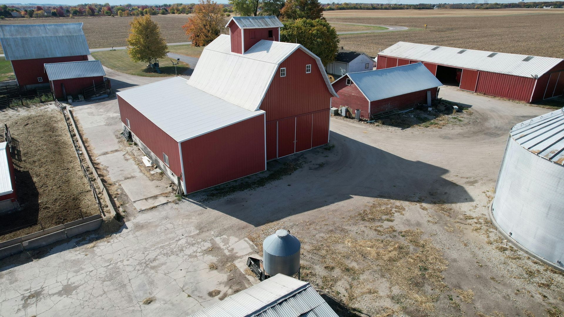 Aerial view of red barns and farm buildings with white roofs and dirt yards in autumn fields