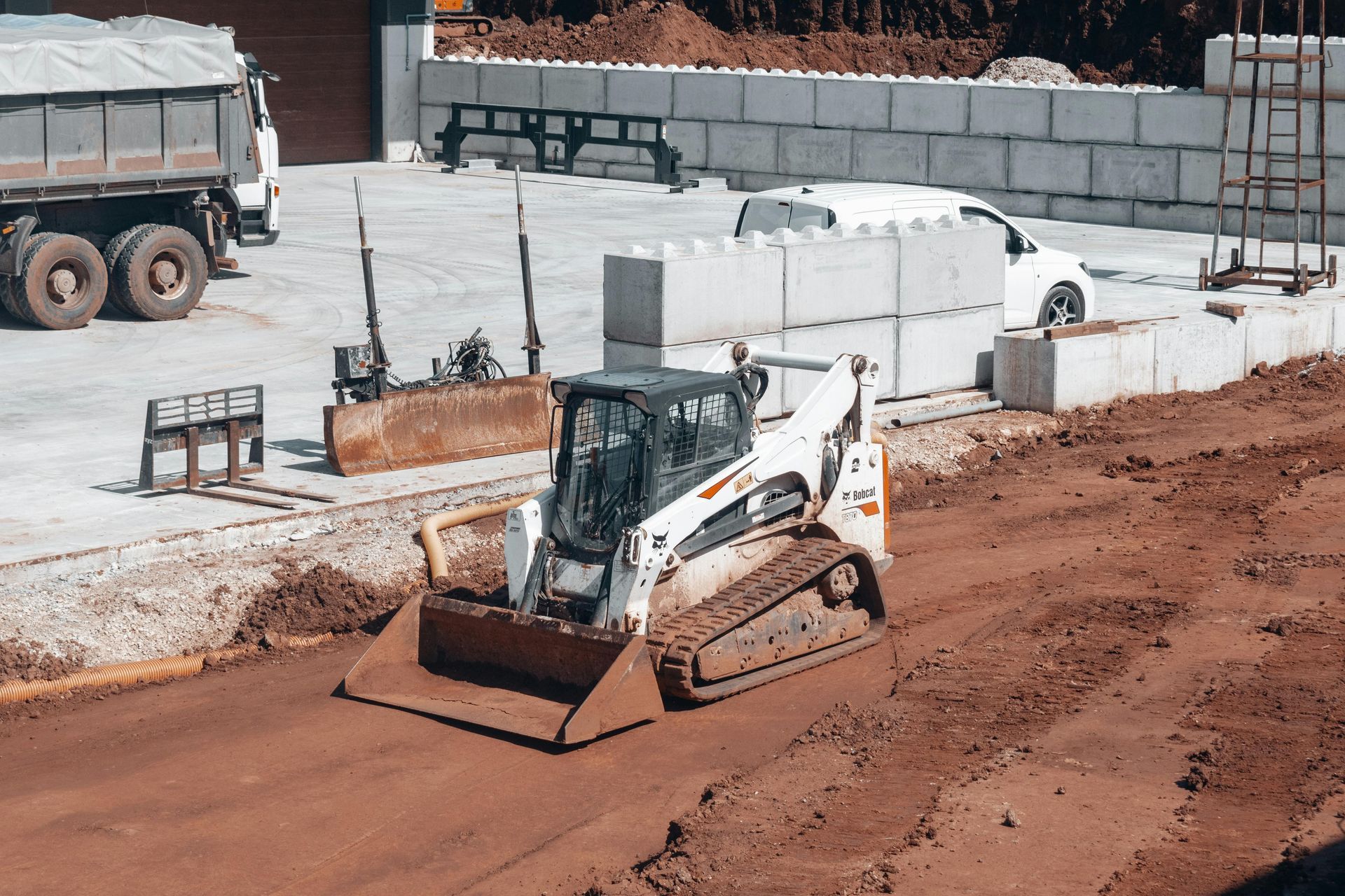 Small bulldozer grading dirt at a construction site beside concrete blocks and trucks