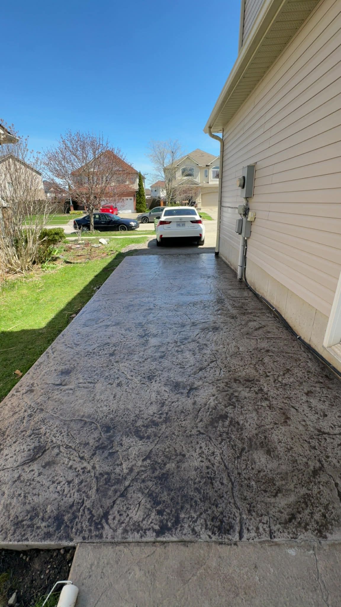 Fresh black gravel driveway beside a beige house, with a white SUV parked ahead under a blue sky.