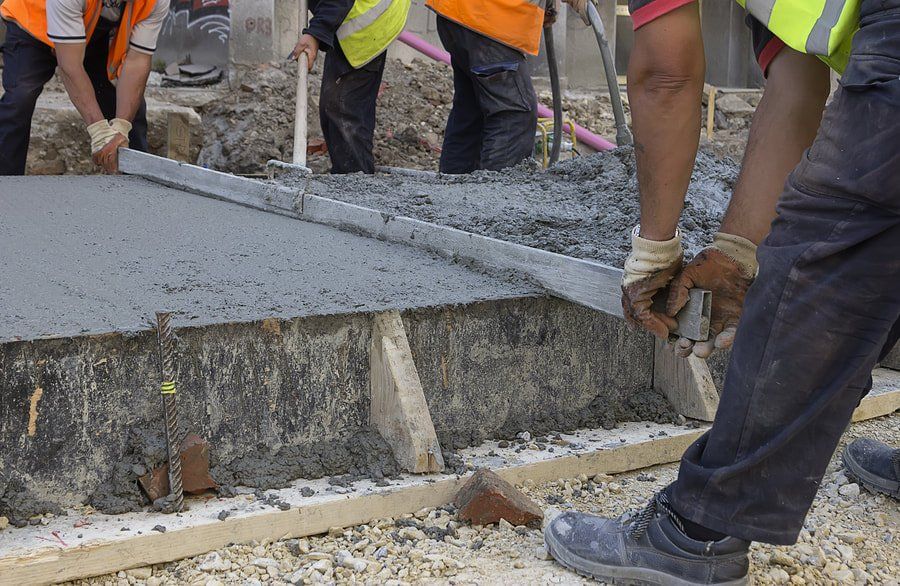 Workers pouring concrete at a construction site, with wet gray concrete and tools visible.