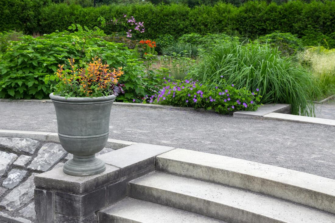 Stone steps beside a gray planter in a lush garden with purple and orange flowers