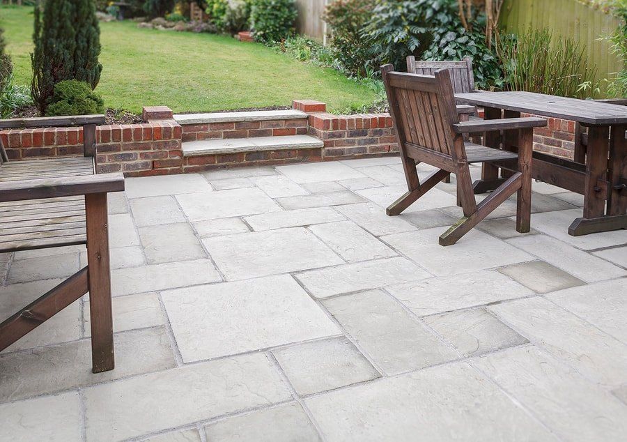 Patio with stone paving, wooden chairs and table, and a low brick wall beside a garden