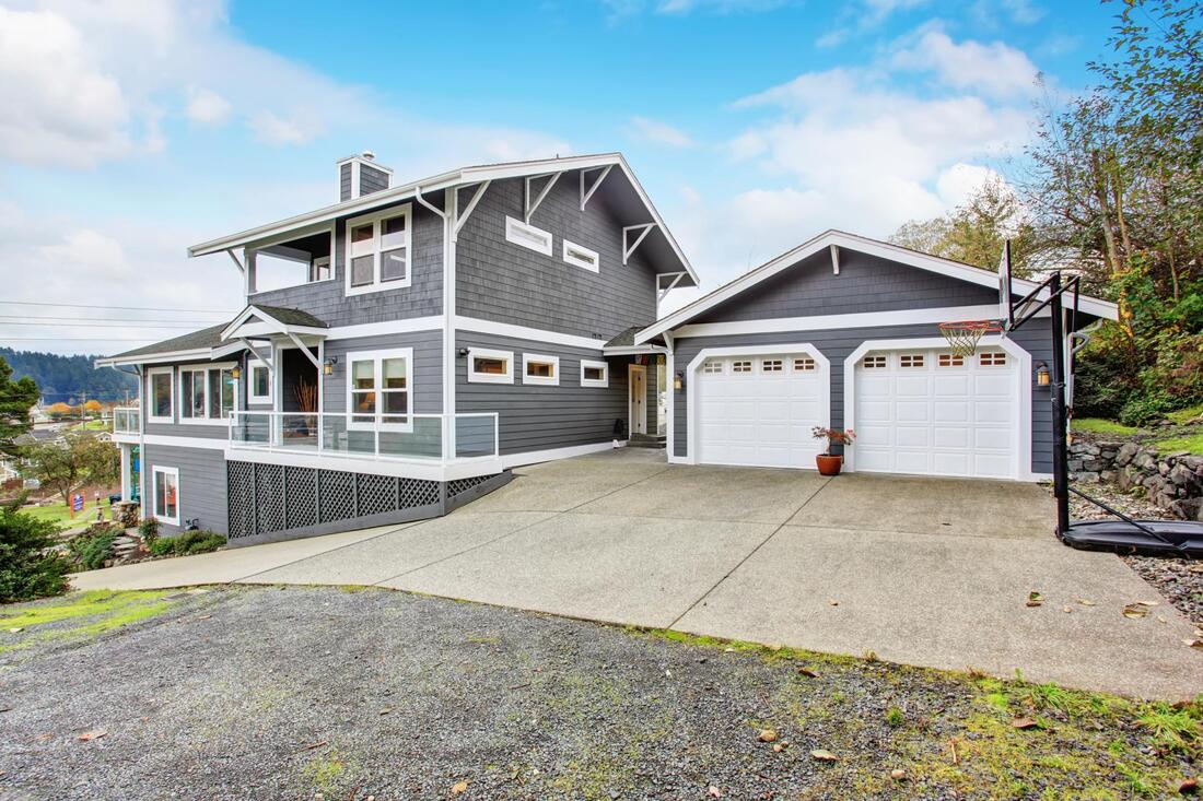 Gray two-story house with white trim and double garage on a sloped driveway