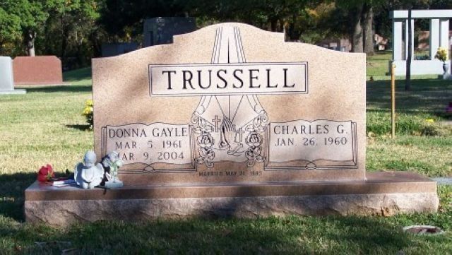 TRUSSELL family gravestone with engraved names in a grassy cemetery, flanked by small floral tributes