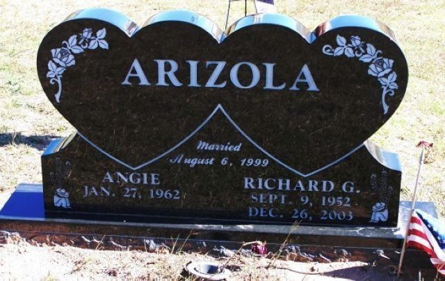 Black heart-shaped gravestone with blue floral designs and the name ARIZOLA in a cemetery