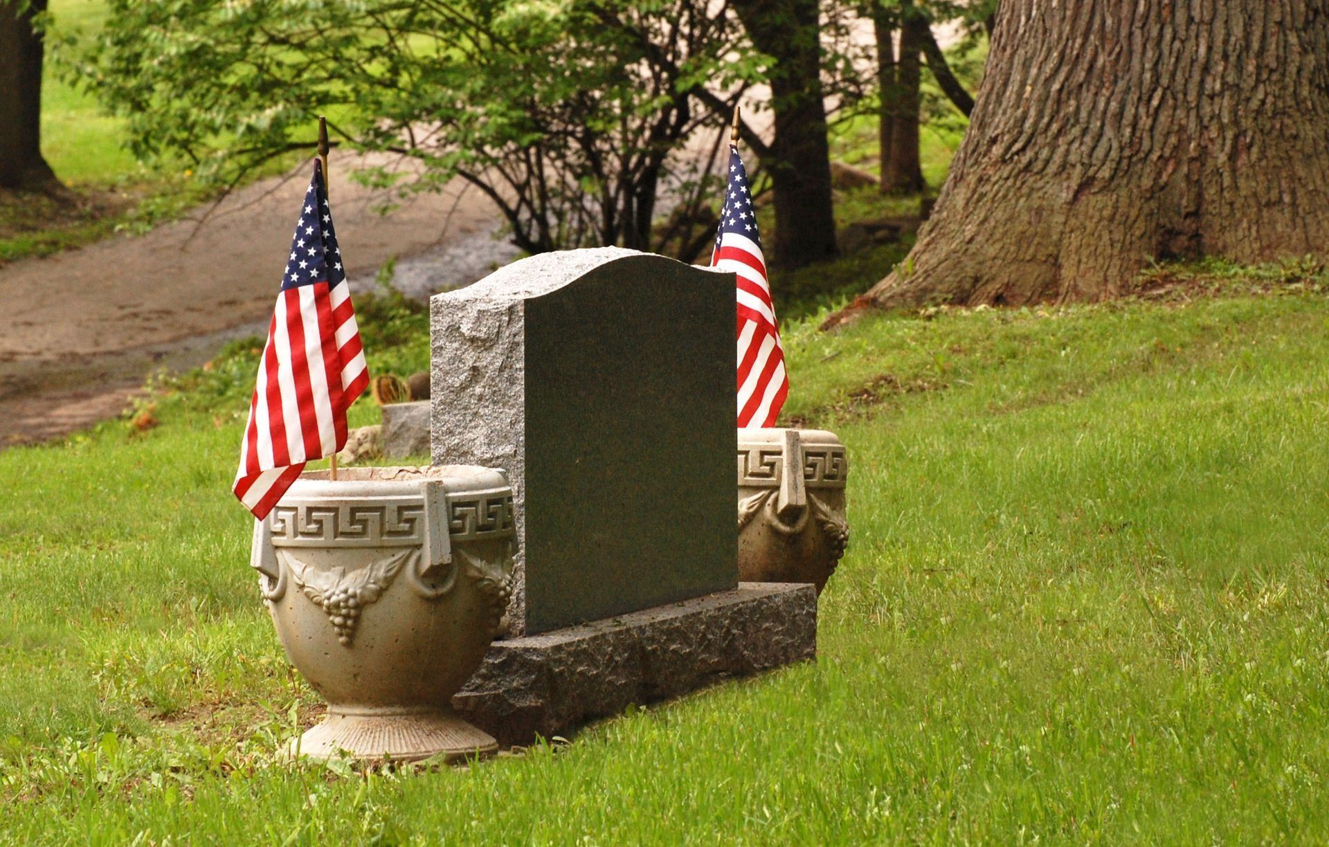 Gravestone in a grassy cemetery with two small American flags and trees in the background