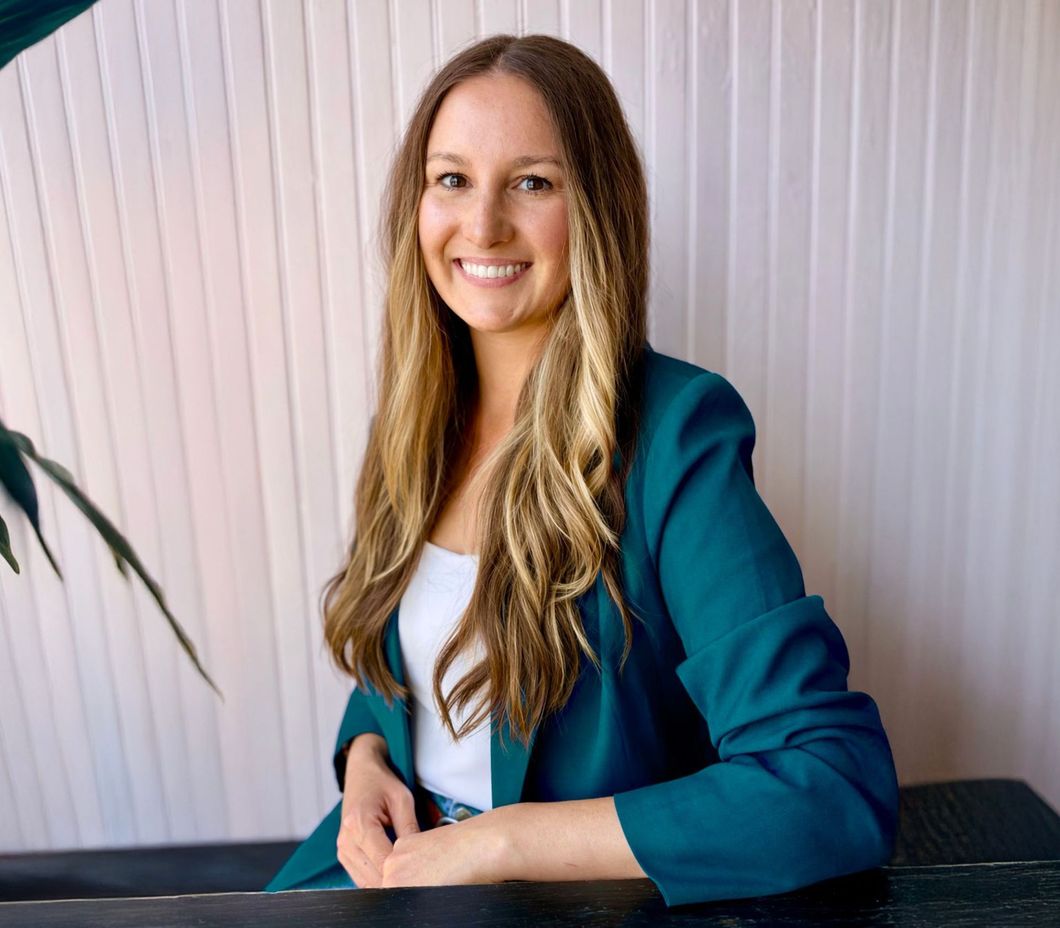 Smiling person in a teal blazer sitting at a table in a bright room