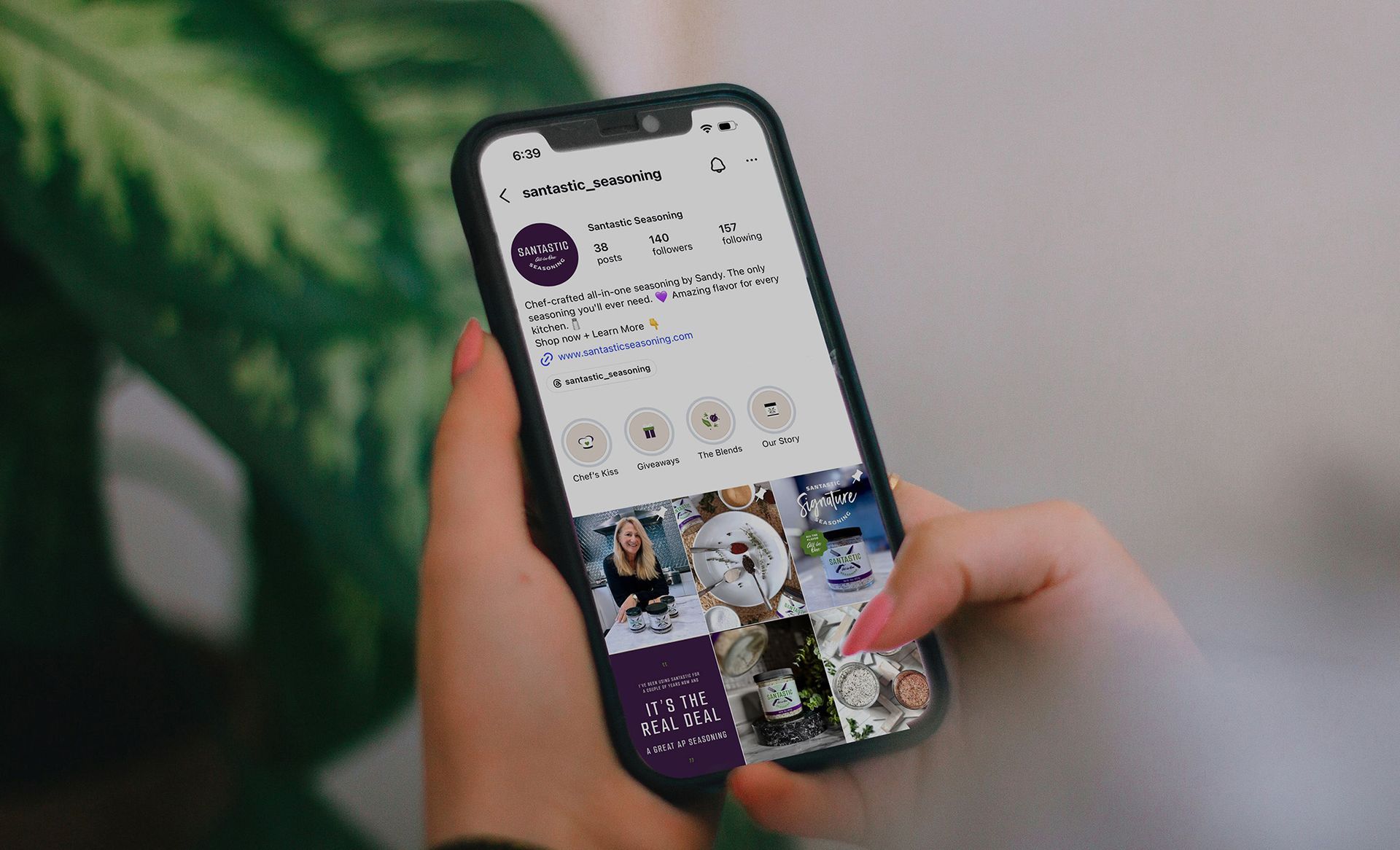 Hands holding a smartphone displaying a social media profile and photo grid
