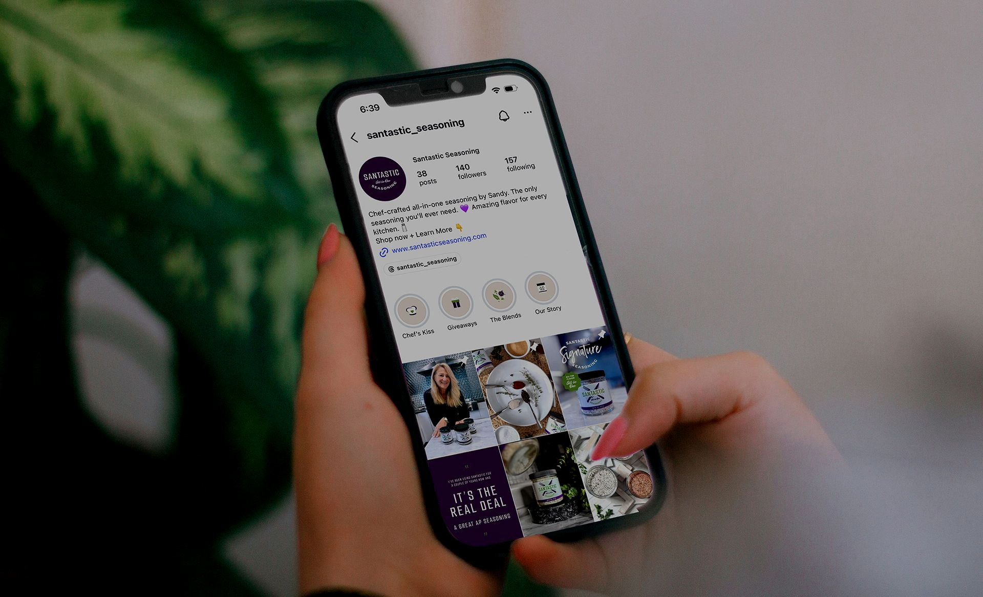 Hands holding a smartphone showing a social media profile page with photos on the screen