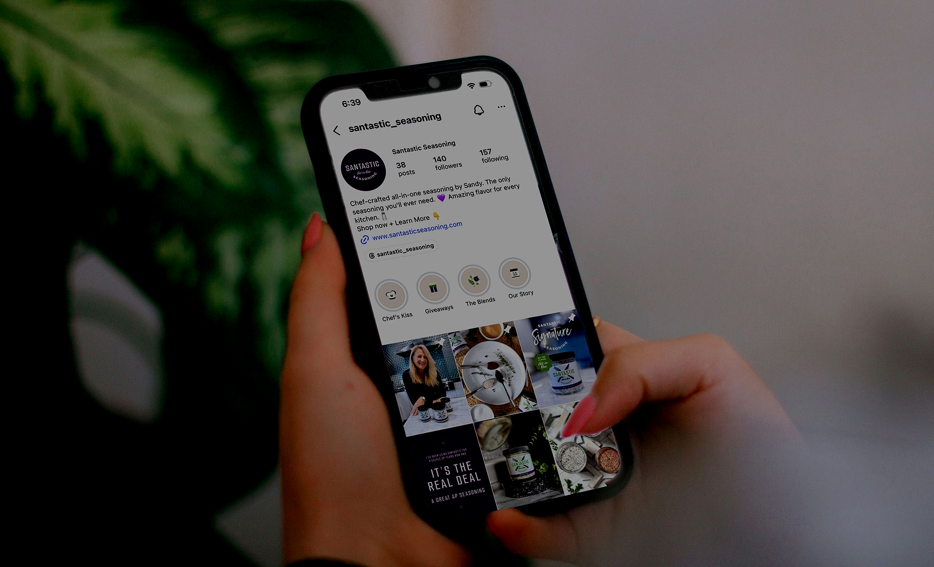 Hands holding a smartphone showing a social media profile and photo grid screen.