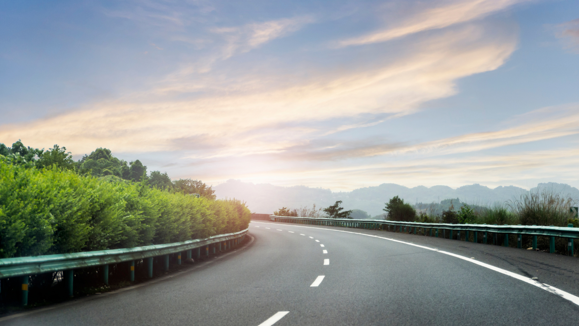 An empty highway with trees on both sides and a sunset in the background.