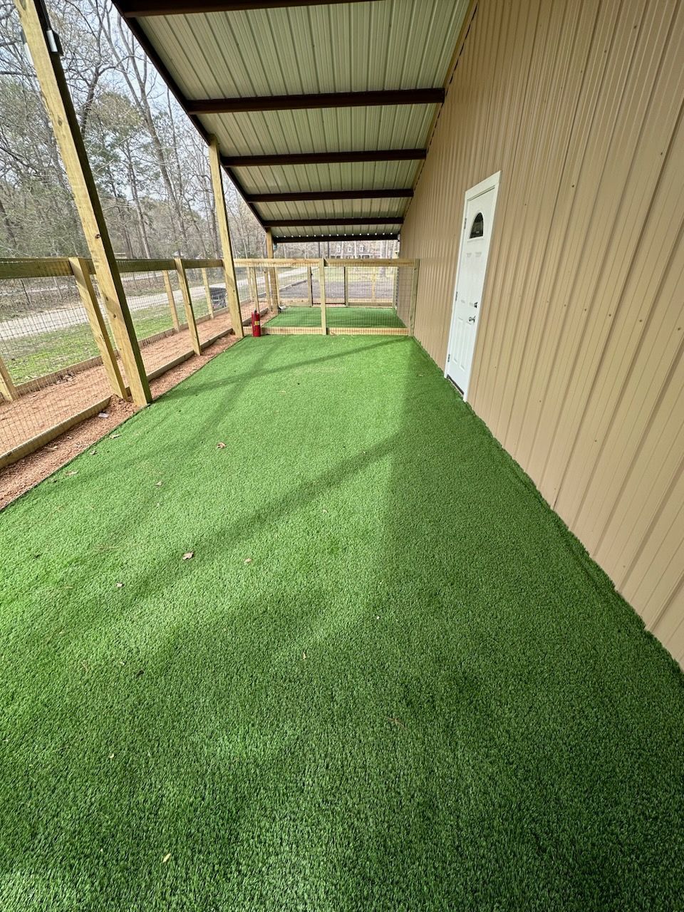 A covered porch with a lot of green grass and a fence.