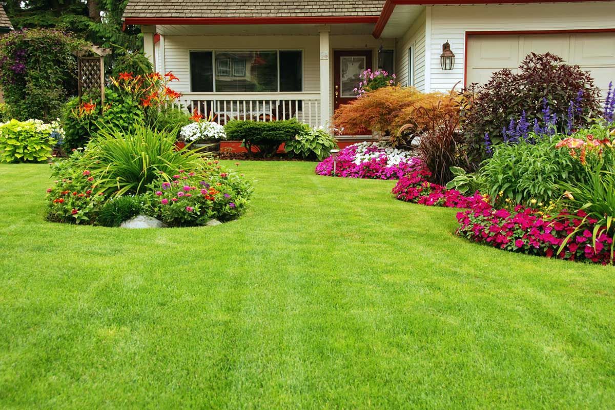 A house with a nicely landscaped, lush green lawn and flowers in front of it.
