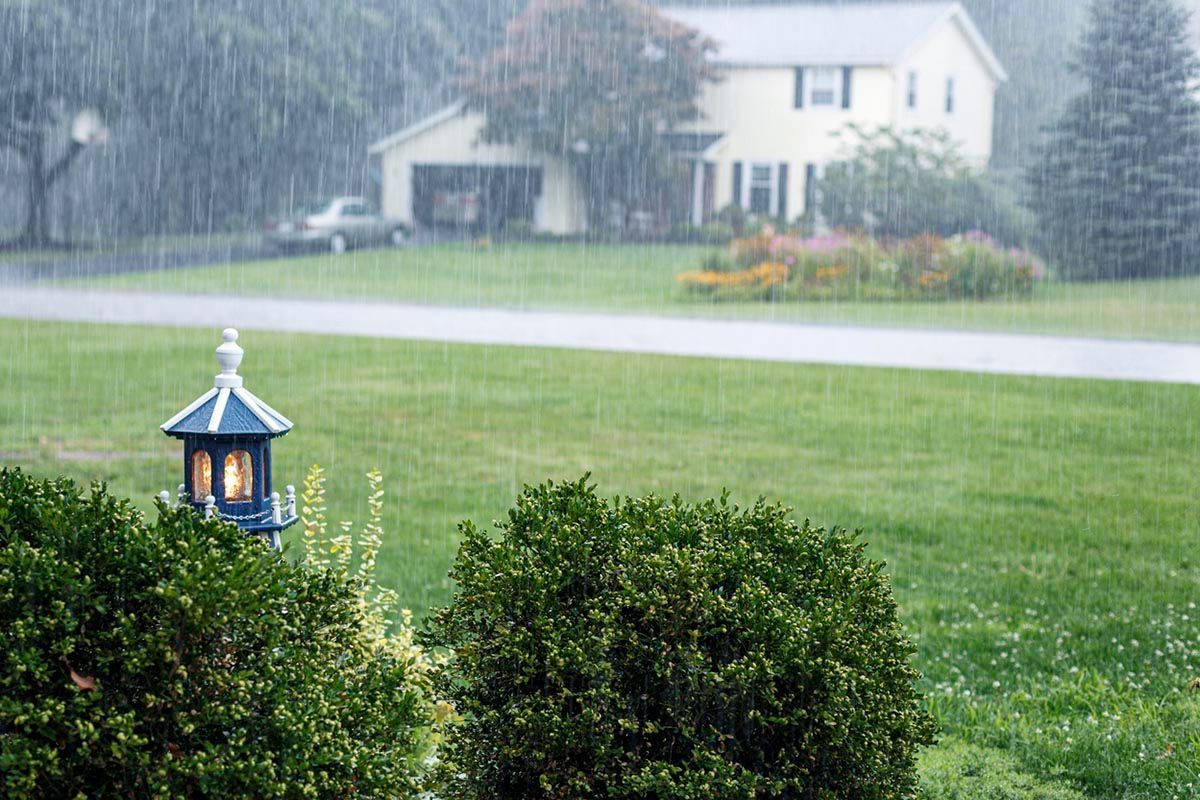 A house is sitting on top of a nicely landscaped, well manicured, lush green field in the rain.