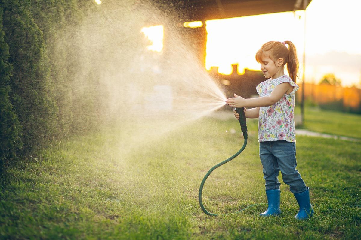 A little girl is watering the grass with a hose.