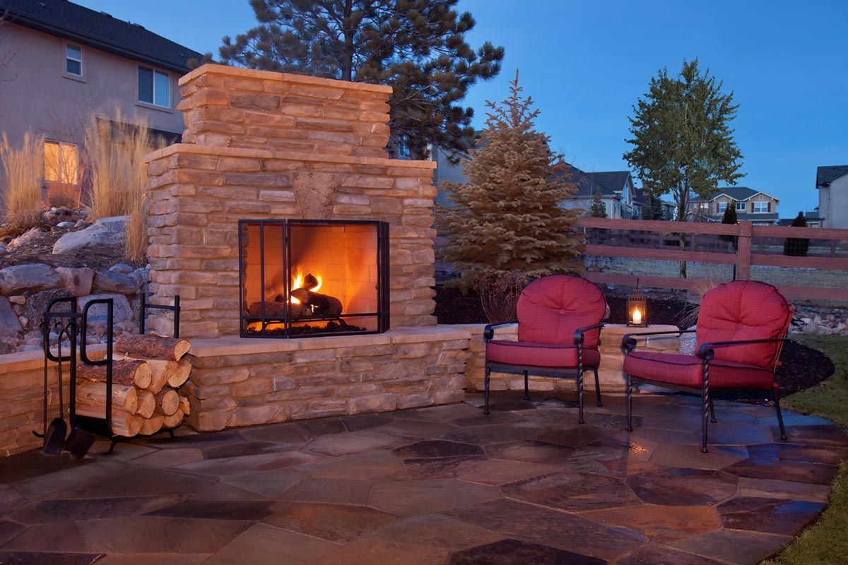 A stone fireplace is lit up in a backyard