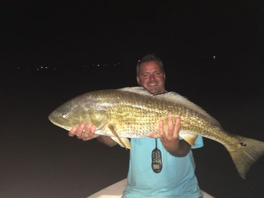 Man holding a large fish at night, smiling in a dark outdoor setting.