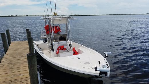 White fishing boat docked by a wooden pier on calm water, with red seats and rods visible.