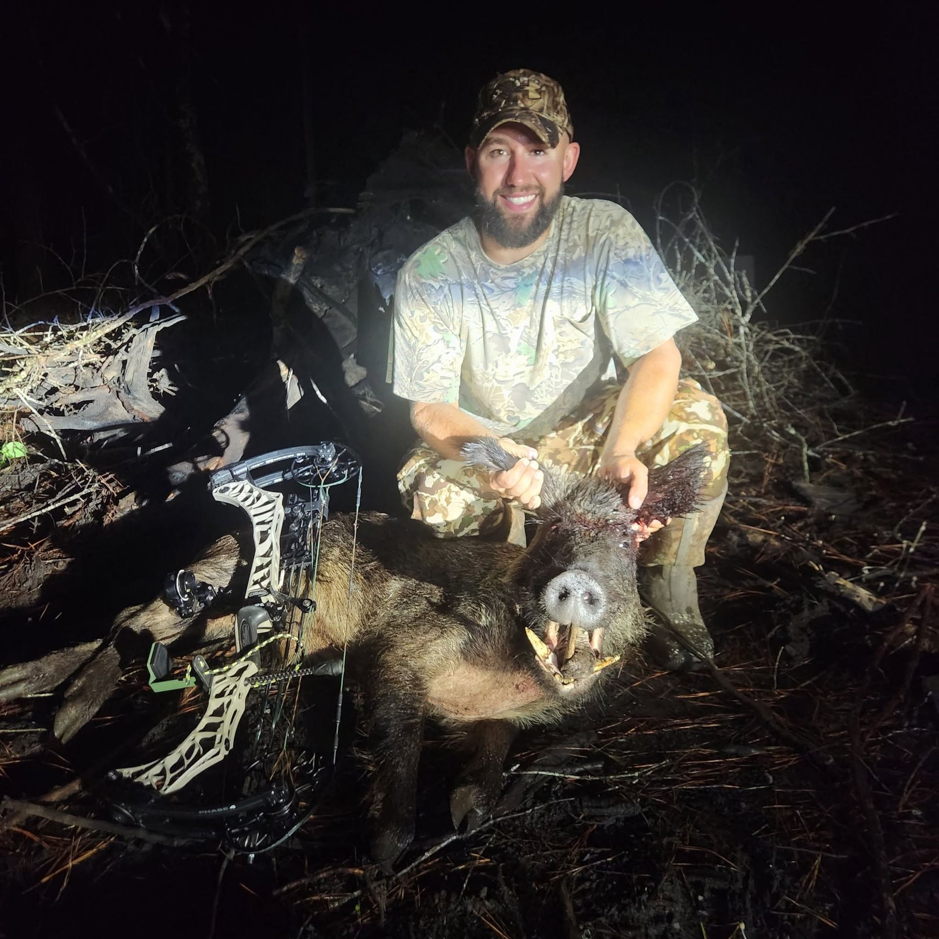 Hunter kneeling at night beside a deer, holding its head, with a bow nearby.
