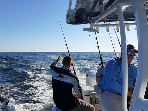 Two people fishing from a boat on rough blue ocean under a clear sky