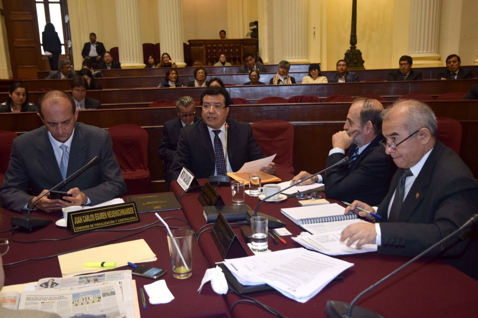 Funcionarios sentados en una mesa de conferencias revisan documentos en una sala de reuniones formal.