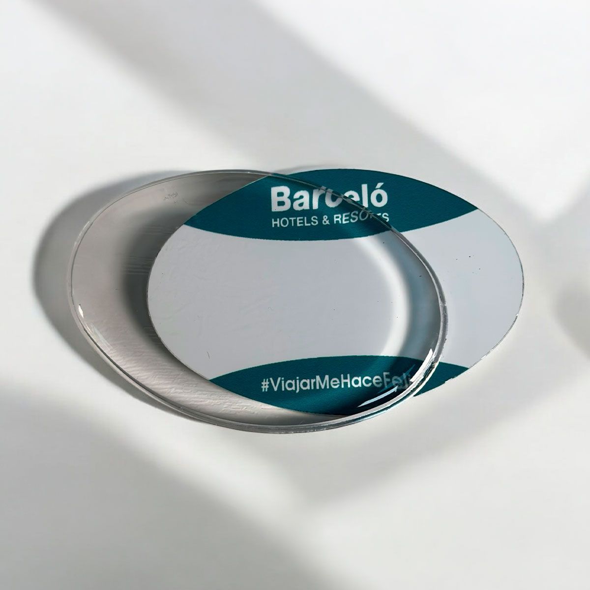 Bandeja ovalada blanca de marca con logotipo y texto en color verde azulado, sobre una superficie gris claro.