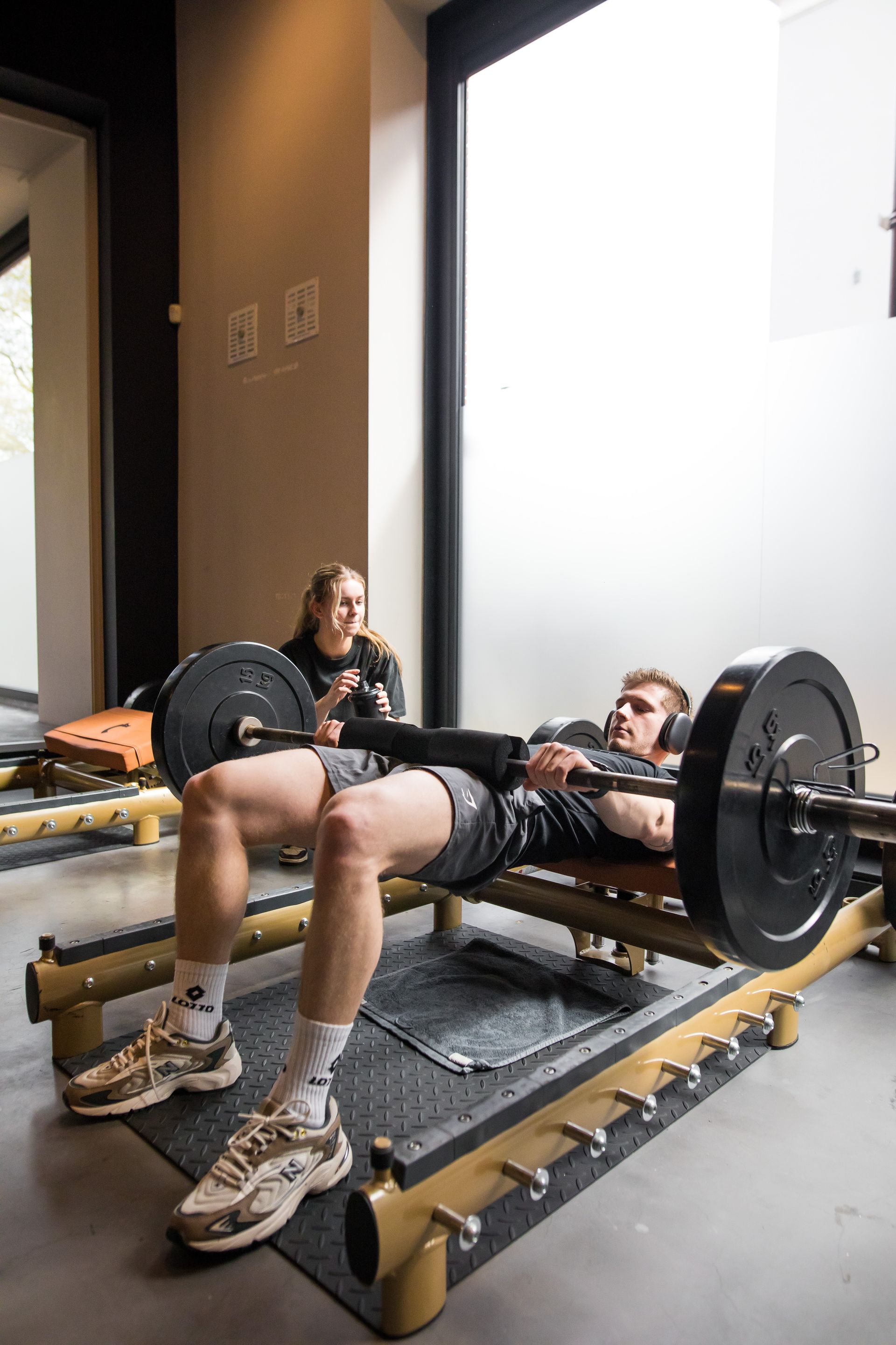 Een man doet squats met een halter op een bankje in een sportschool.