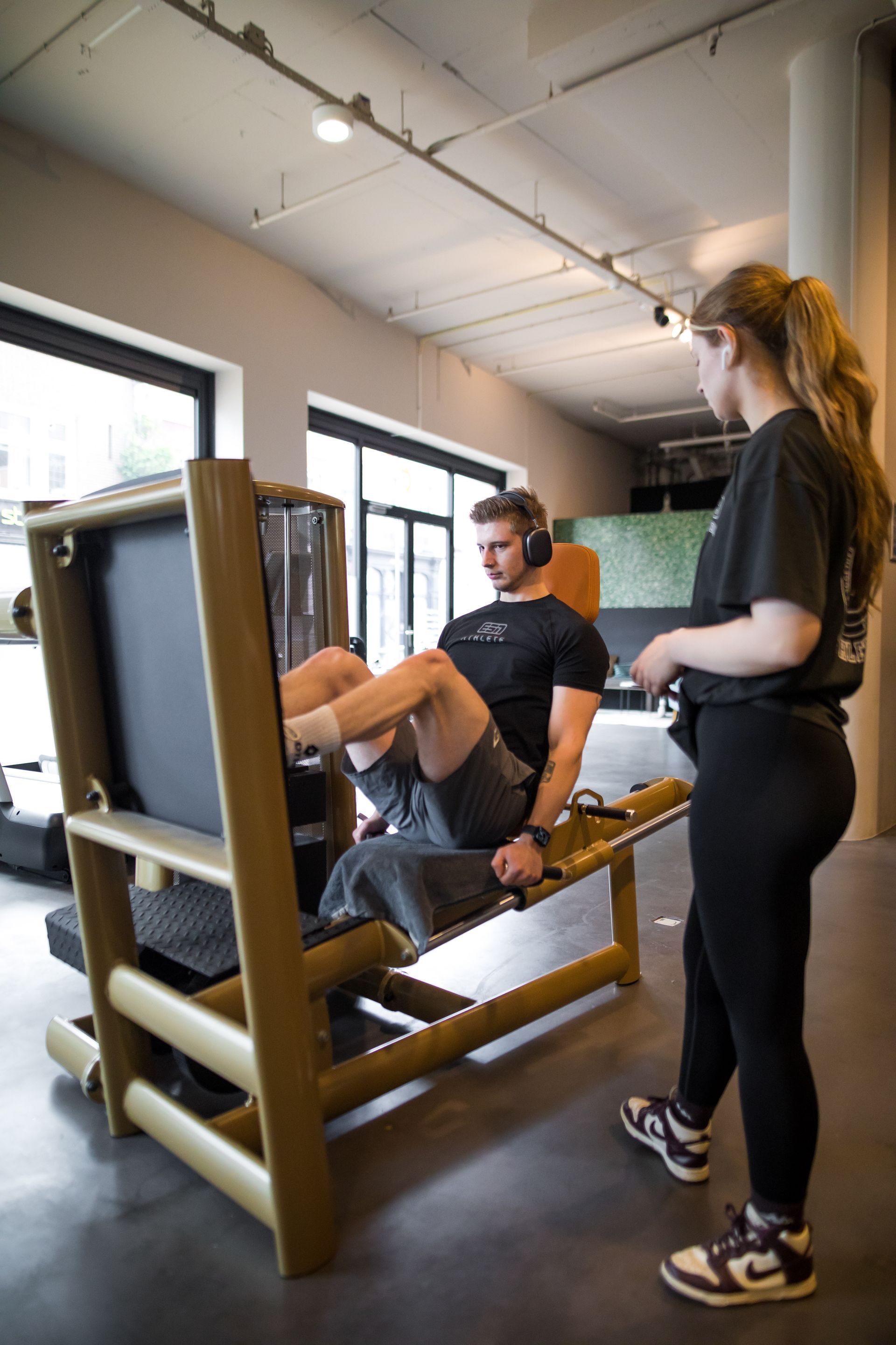 Een man gebruikt een legpressmachine in een sportschool terwijl een vrouw toekijkt.