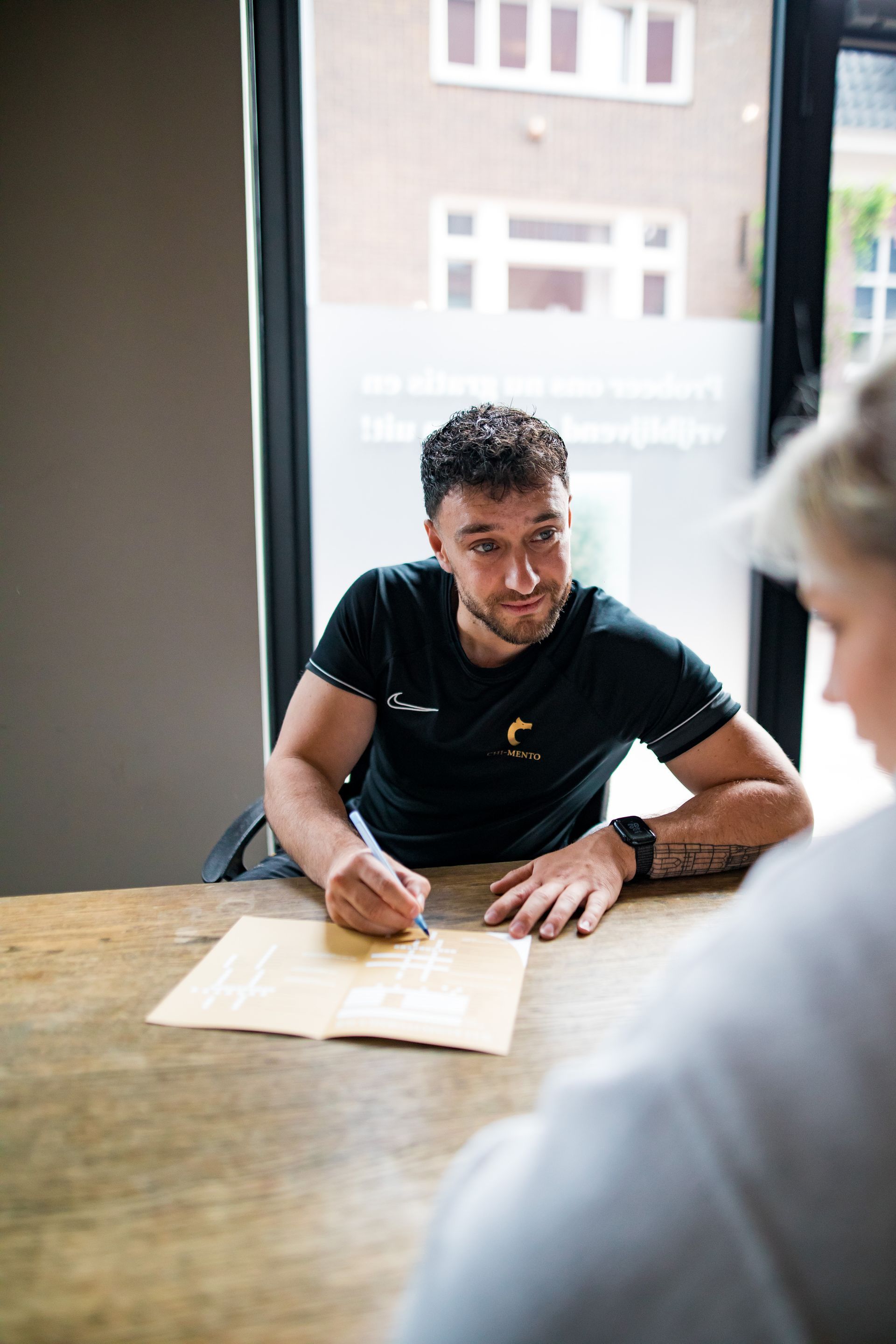 Een man zit aan een tafel en schrijft op een stuk papier.
