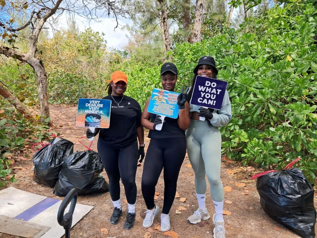 Three young women holding signs pose next to trash bags after a cleanup. 